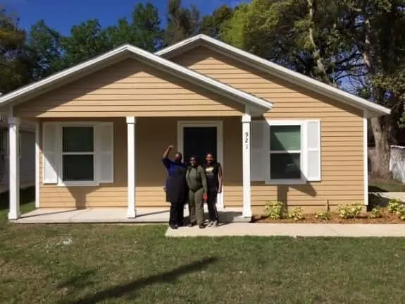 Homeowner Latoya poses in front of her brown home with two family members.