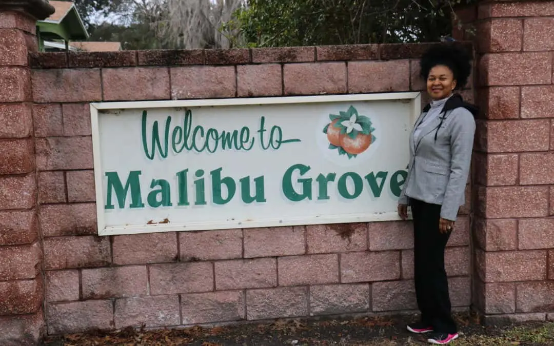 Woman smiling in front of brick wall and "Welcome to Malibu Groves" sign