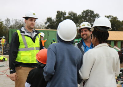 Two men talking with family in front of in-progress houses