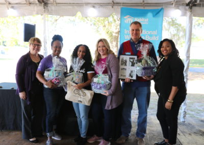 Five women and a man holding wrapped gift baskets and smiling