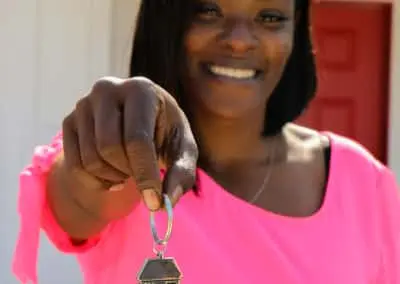 Woman smiling in front of red door holding out house-shaped keychain