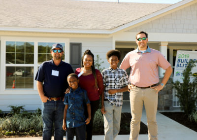 Woman with her two sons and two men smiling and standing in front of newly completed house