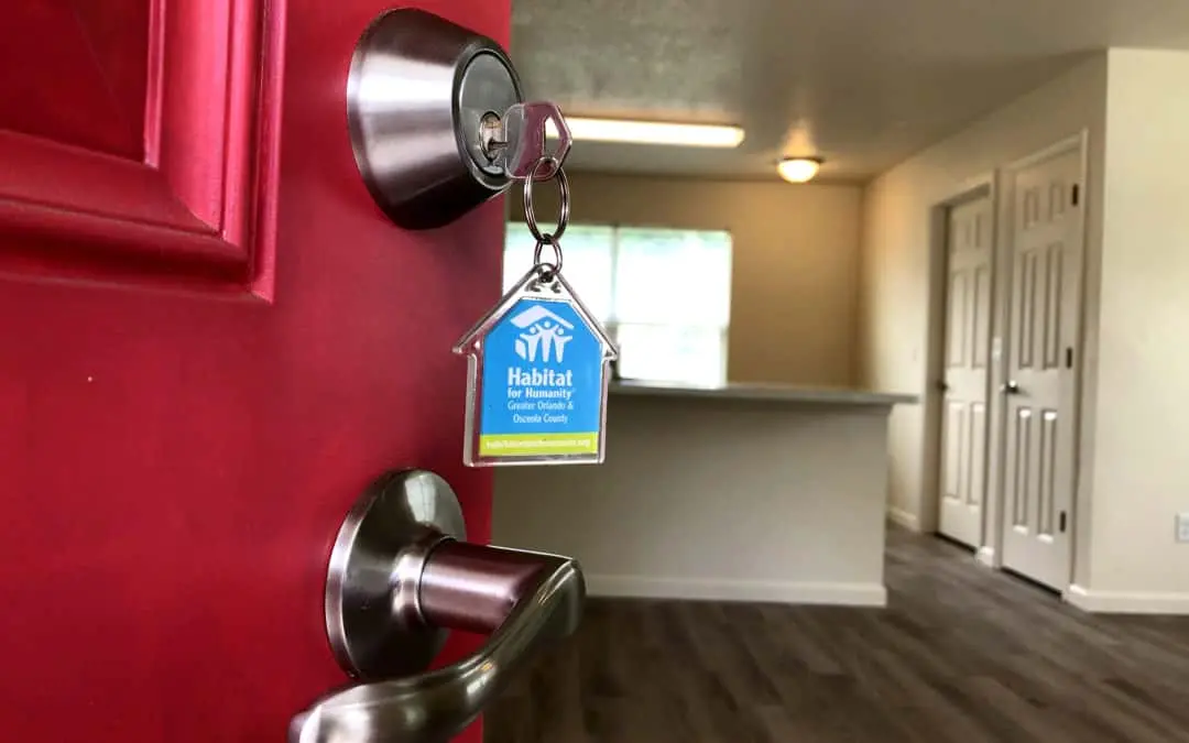 A red door opens into a Habitat home. A Habitat keychain is in the lock.