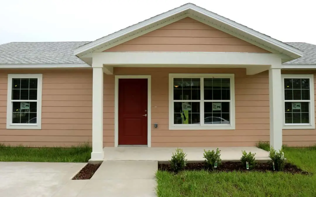 A photo of a peach house with a red door and white trim.