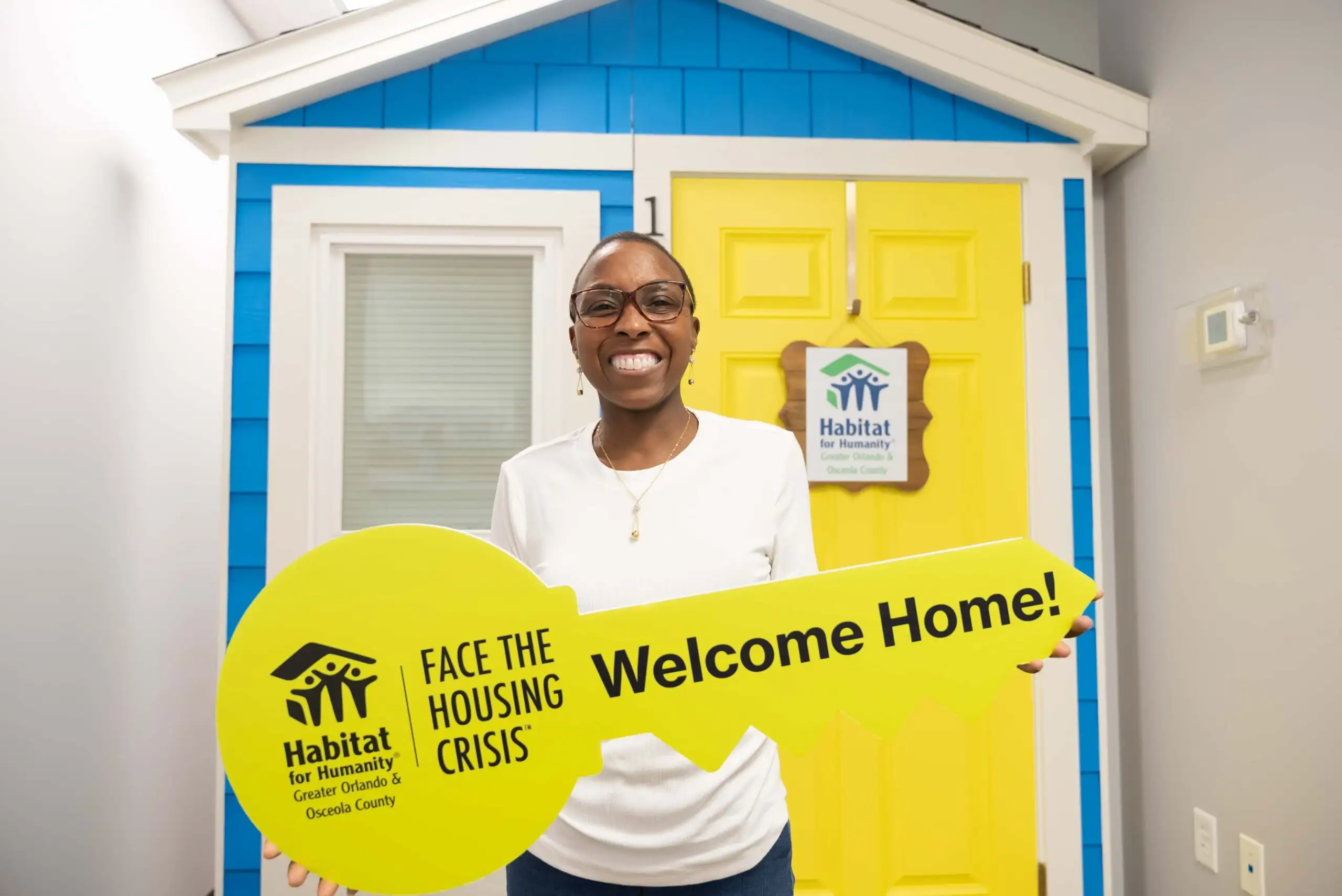 A smiling woman poses with house keys in front of her home.